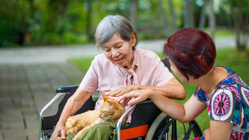 An elderly woman in a wheelchair holding her caretaker's hand.